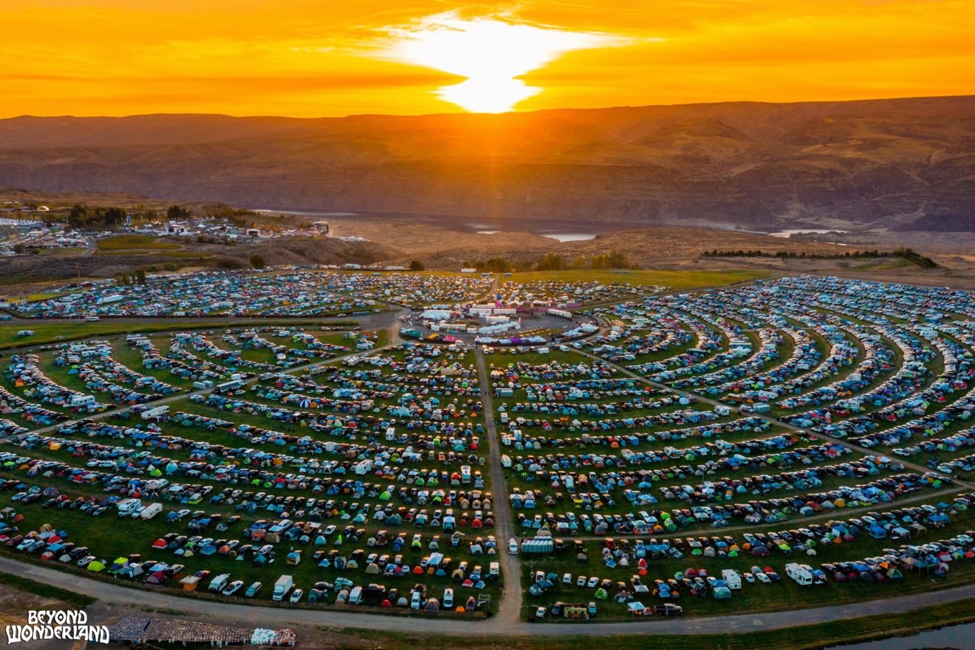 An overhead view of a large campground with overlooking a river with the sun setting in the background.