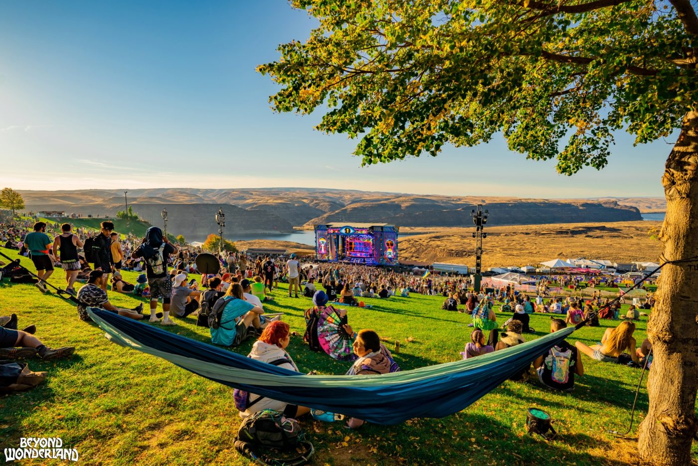 People sitting in hammock, overlooking a hill, a stage, and a river beyond it.