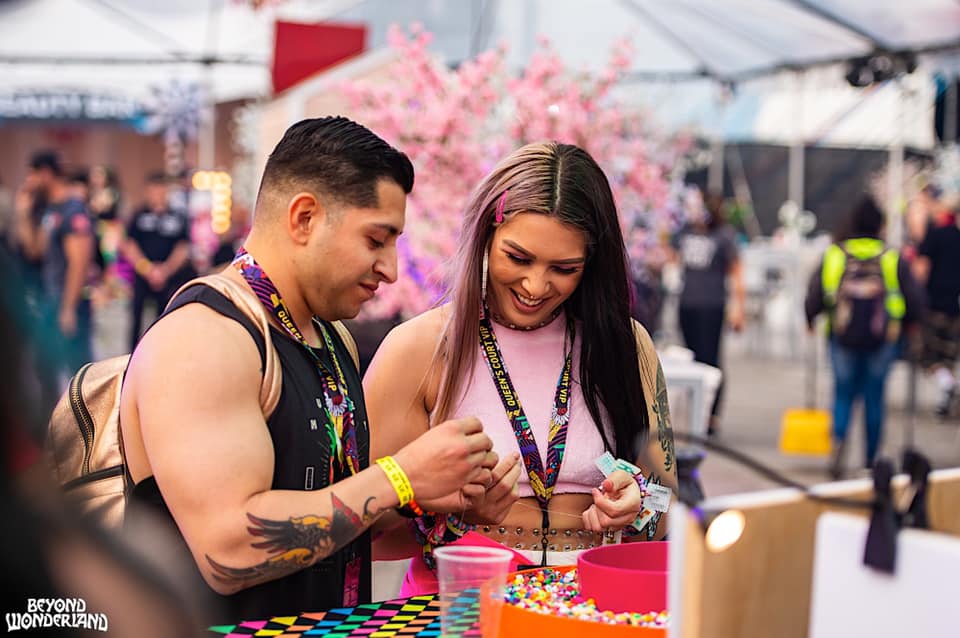 Two people making beaded bracelets and smiling.